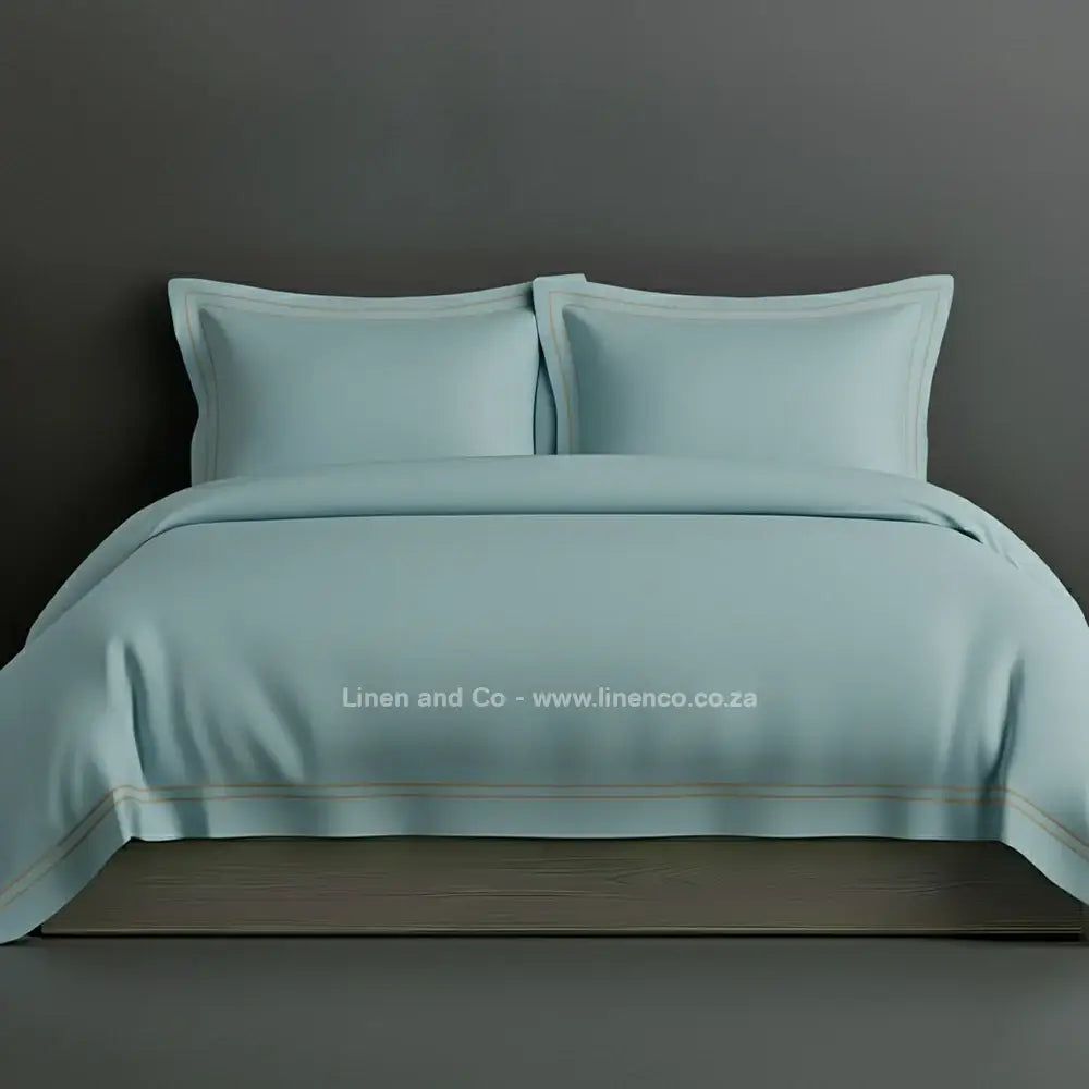 Duck egg percale duvet cover set with Oxford two-row white satin stitch border from Linen and Co, showcasing elegant hospitality bedding with subtle decorative detailing against a dark grey background.