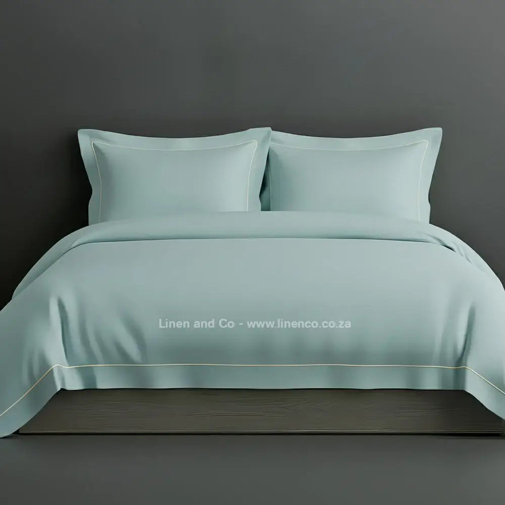 Duck Egg percale duvet cover set with Oxford one-row white satin stitch border from Linen and Co, showcasing elegant hospitality bedding with subtle decorative detailing against a dark grey background.