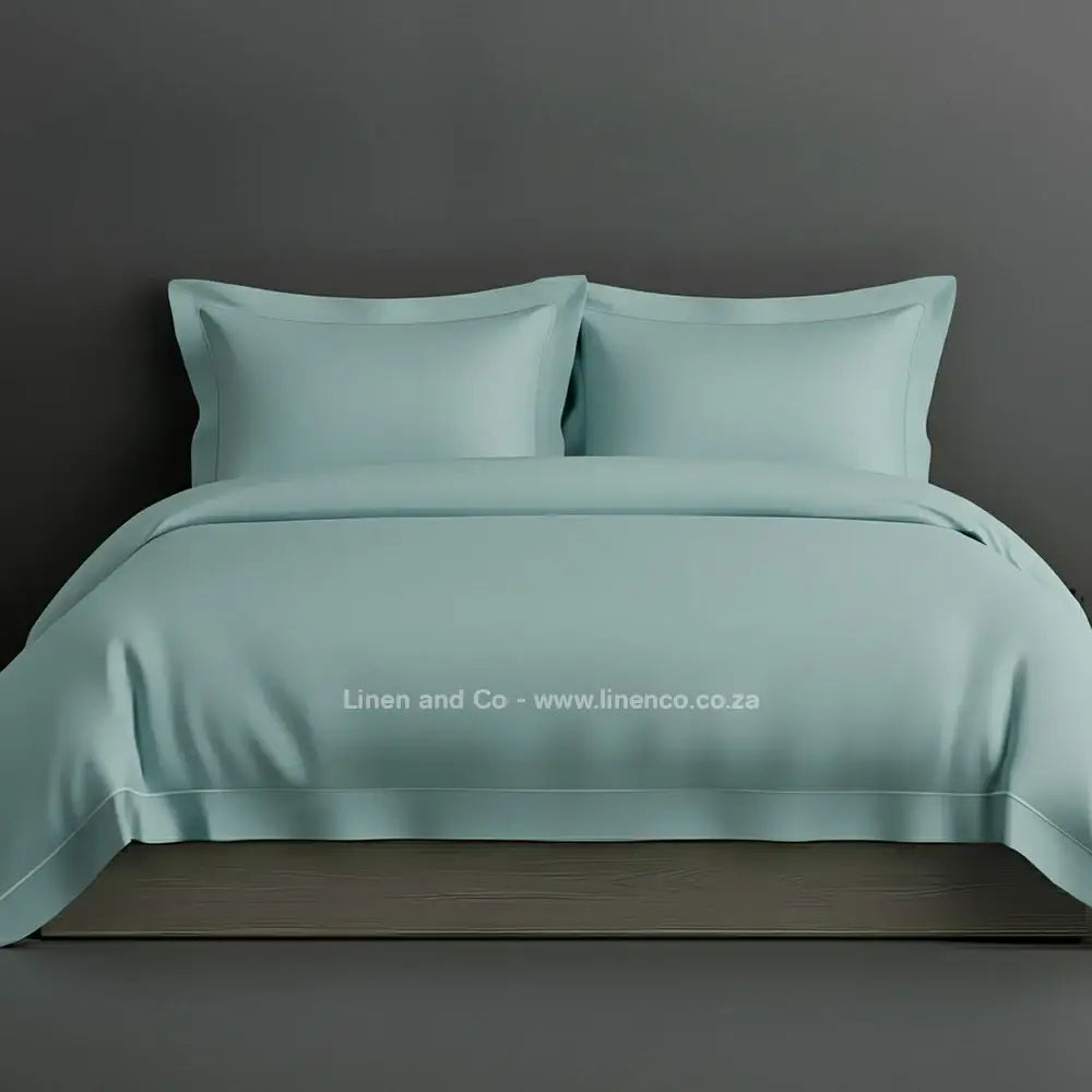 Duck Egg percale duvet cover set with Oxford one-row white satin stitch border from Linen and Co, showcasing elegant hospitality bedding with subtle decorative detailing against a dark grey background.