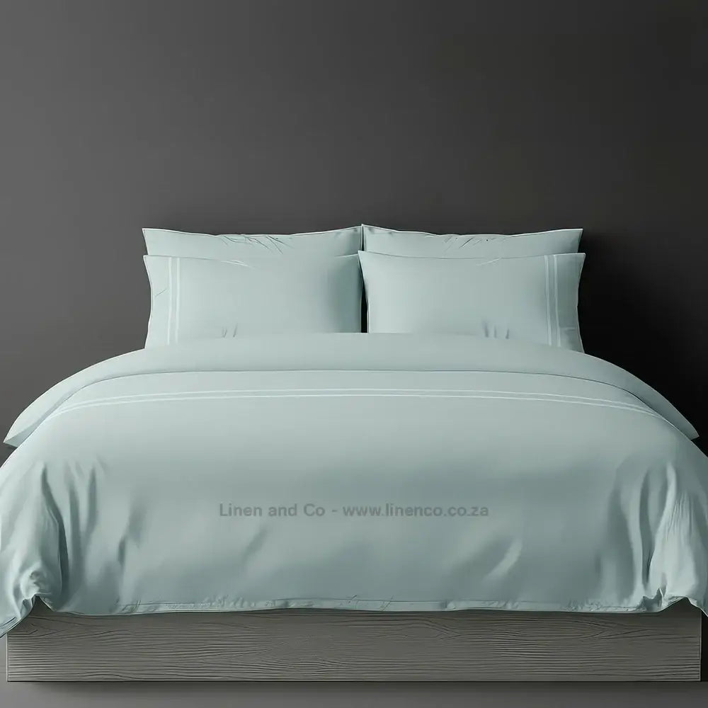 Duck Egg percale duvet cover set with two-row white satin stitch border from Linen and Co, showcasing elegant hospitality bedding with subtle decorative detailing against a dark grey background.