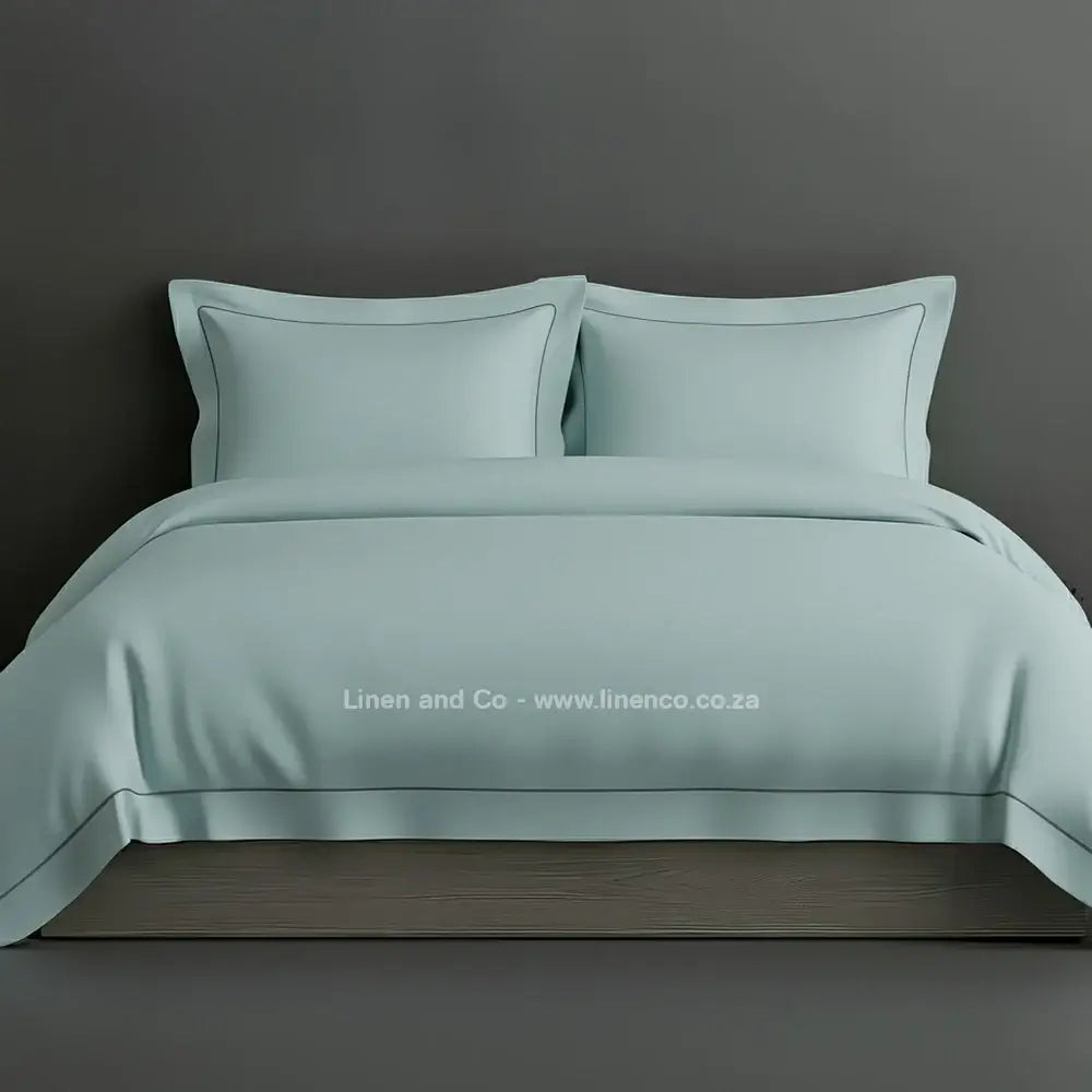 Duck Egg percale duvet cover set with Oxford one-row white satin stitch border from Linen and Co, showcasing elegant hospitality bedding with subtle decorative detailing against a dark grey background.
