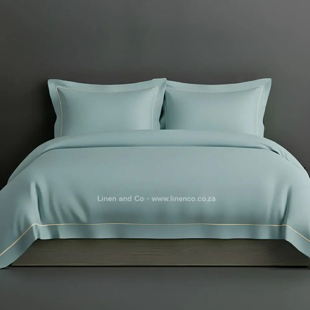 Duck Egg percale duvet cover set with Oxford one-row white satin stitch border from Linen and Co, showcasing elegant hospitality bedding with subtle decorative detailing against a dark grey background.