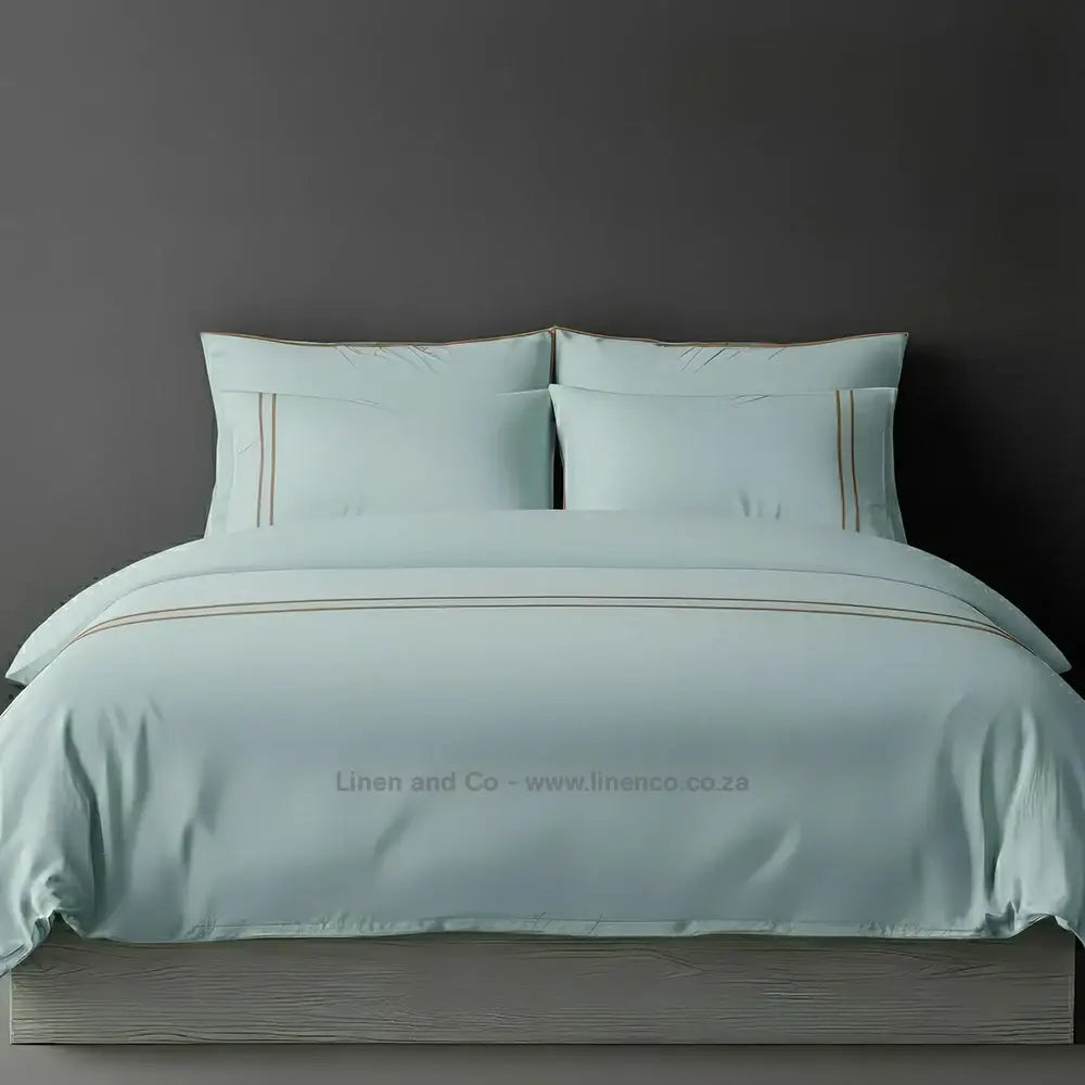 Duck Egg percale duvet cover set with two-row white satin stitch border from Linen and Co, showcasing elegant hospitality bedding with subtle decorative detailing against a dark grey background.