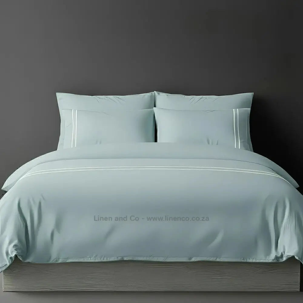 Duck Egg  percale duvet cover set with two-row white satin stitch border from Linen and Co, showcasing elegant hospitality bedding with subtle decorative detailing against a dark grey background.