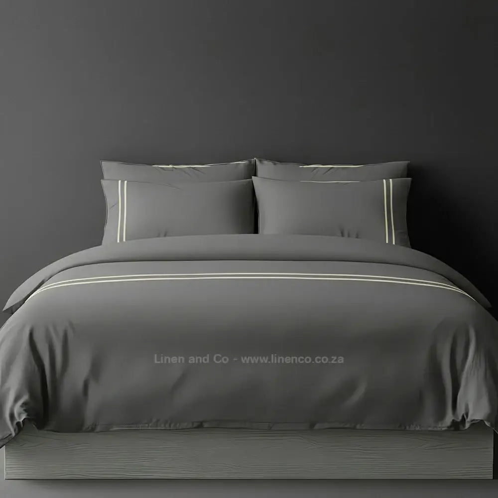 Grey percale duvet cover set with two-row white satin stitch border from Linen and Co, showcasing elegant hospitality bedding with subtle decorative detailing against a dark grey background.