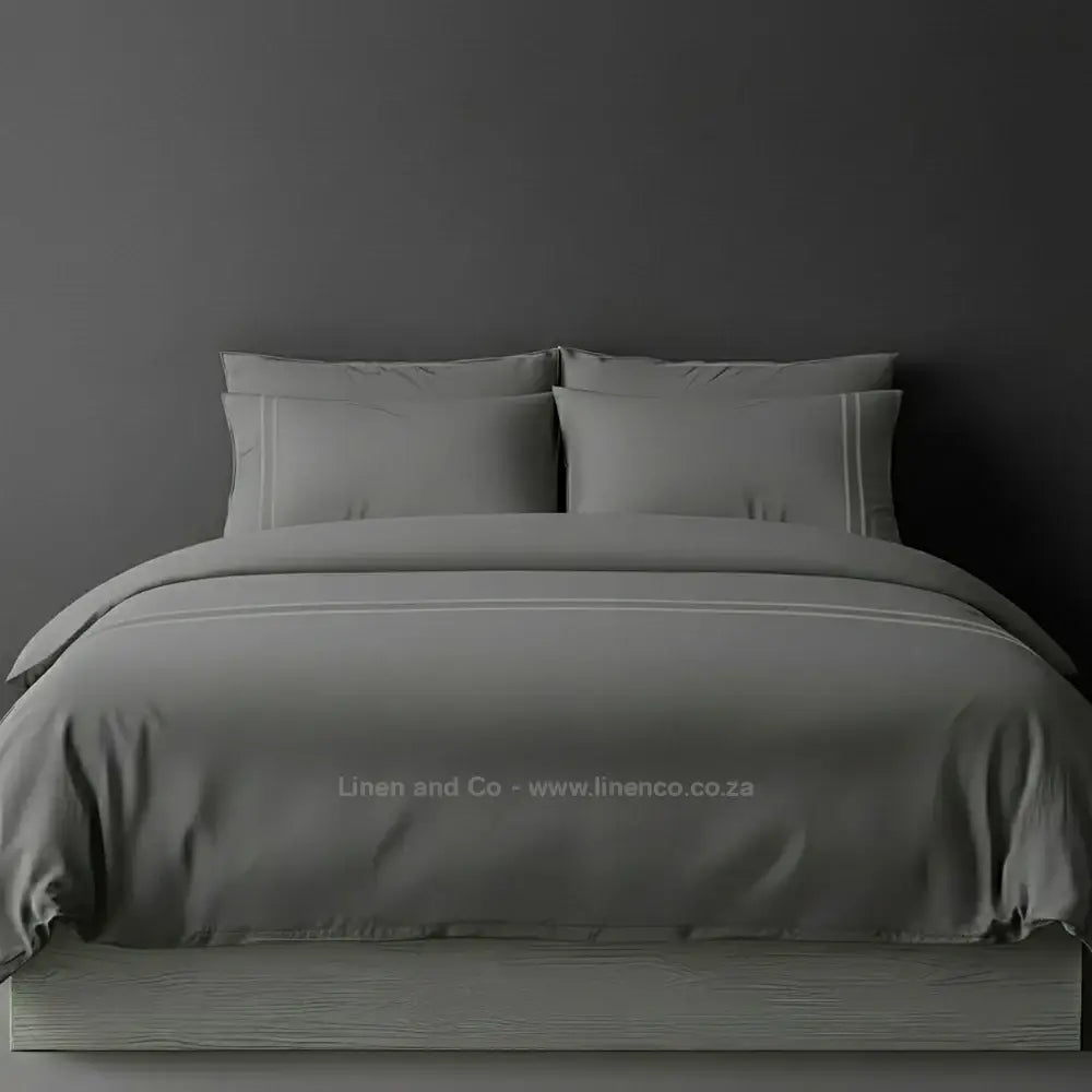 Grey percale duvet cover set with two-row white satin stitch border from Linen and Co, showcasing elegant hospitality bedding with subtle decorative detailing against a dark grey background.