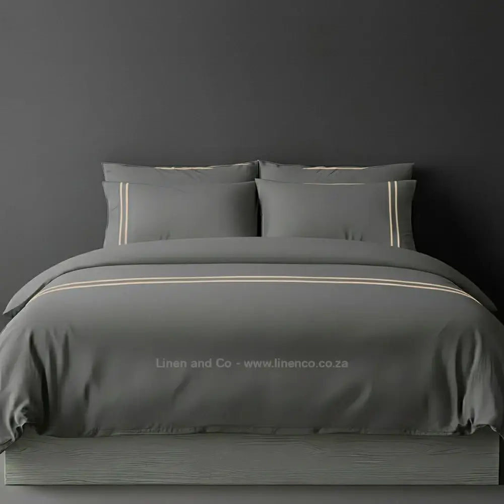 Grey percale duvet cover set with two-row white satin stitch border from Linen and Co, showcasing elegant hospitality bedding with subtle decorative detailing against a dark grey background.