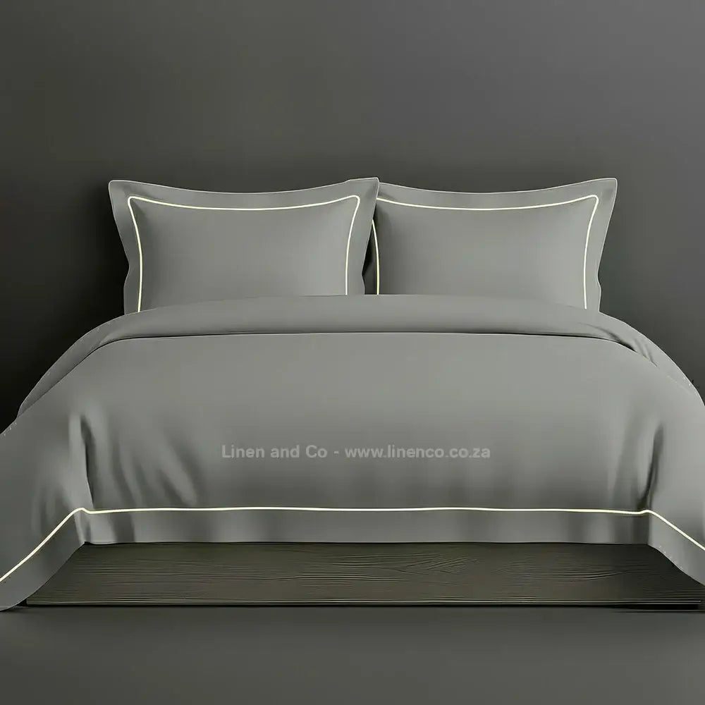 Grey percale duvet cover set with Oxford one-row white satin stitch border from Linen and Co, showcasing elegant hospitality bedding with subtle decorative detailing against a dark grey background.