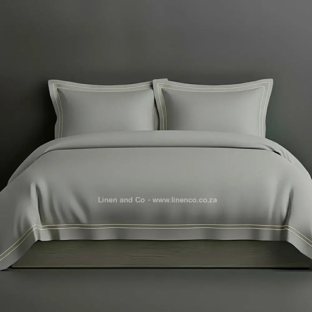 Grey percale duvet cover set with Oxford two-row white satin stitch border from Linen and Co, showcasing elegant hospitality bedding with subtle decorative detailing against a dark grey background.