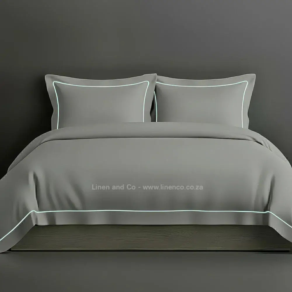 Duck Egg percale duvet cover set with Oxford one-row white satin stitch border from Linen and Co, showcasing elegant hospitality bedding with subtle decorative detailing against a dark grey background.