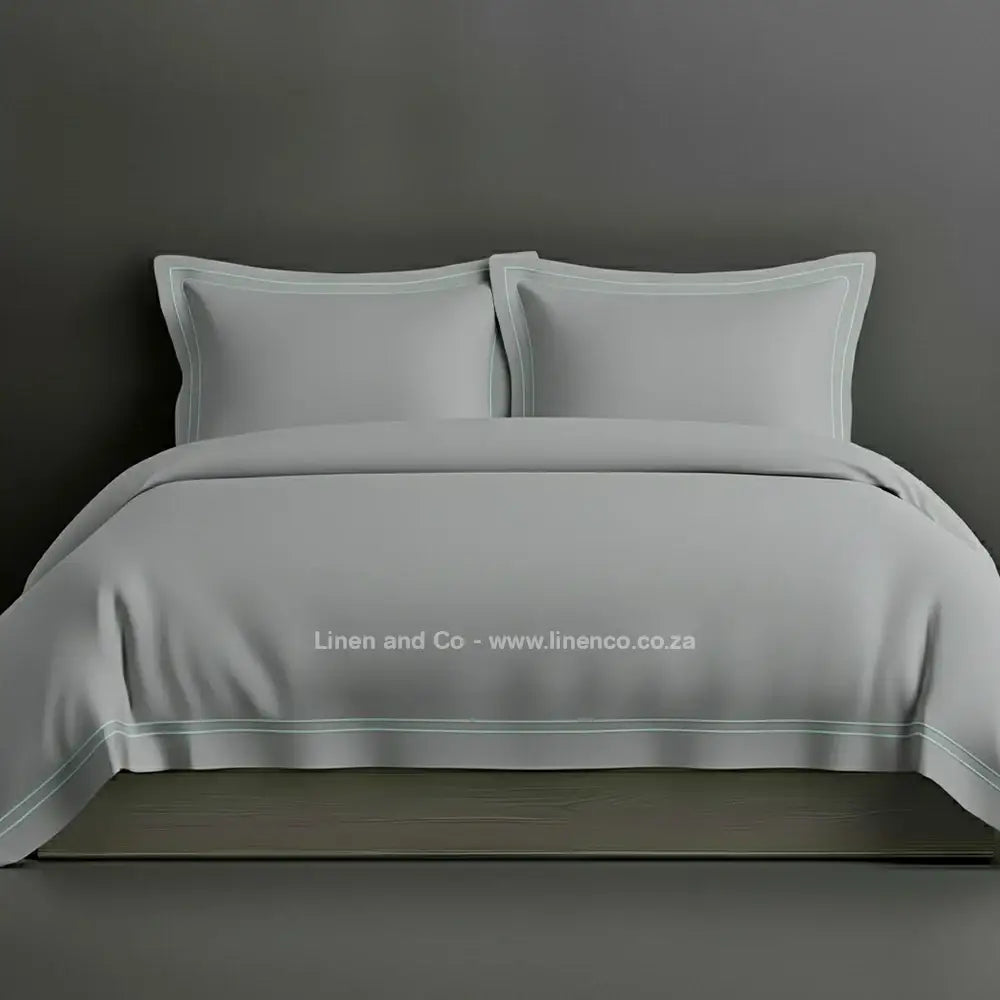 Grey percale duvet cover set with Oxford two-row white satin stitch border from Linen and Co, showcasing elegant hospitality bedding with subtle decorative detailing against a dark grey background.