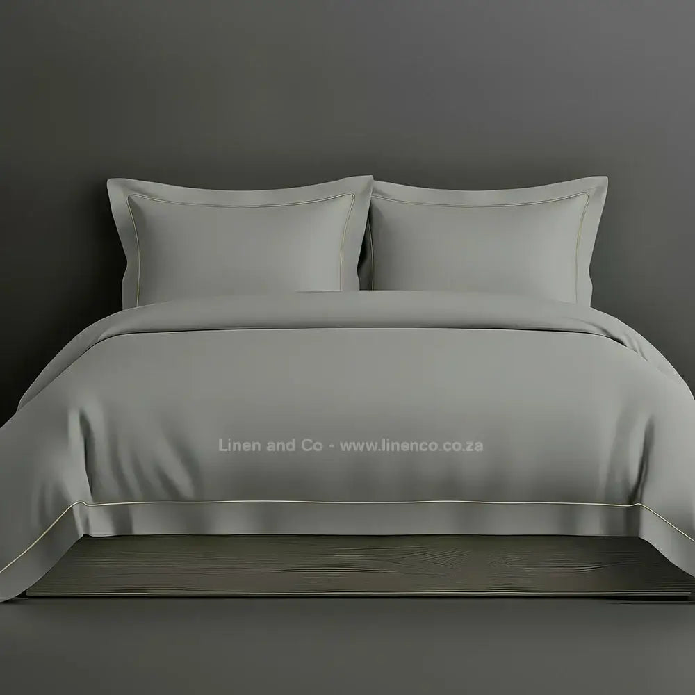 Grey percale duvet cover set with Oxford one-row white satin stitch border from Linen and Co, showcasing elegant hospitality bedding with subtle decorative detailing against a dark grey background.