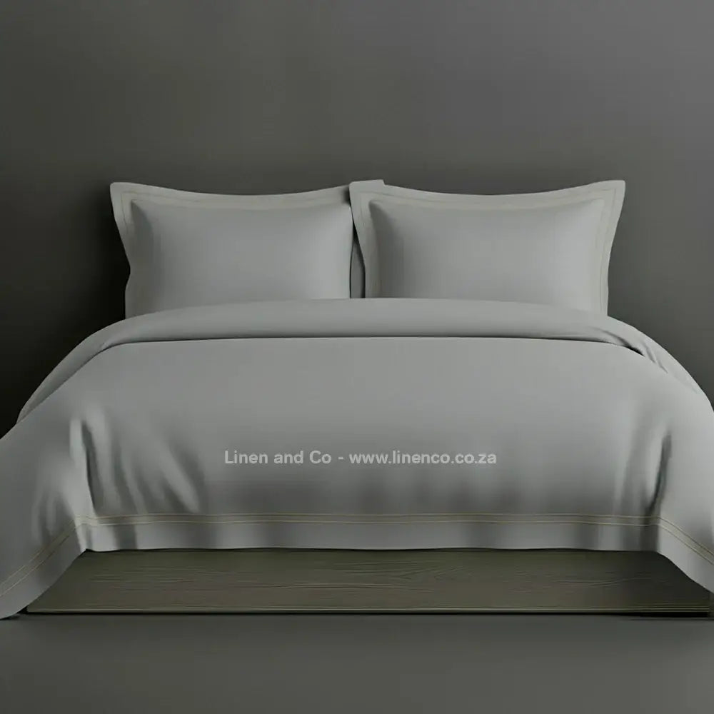 Grey percale duvet cover set with Oxford two-row white satin stitch border from Linen and Co, showcasing elegant hospitality bedding with subtle decorative detailing against a dark grey background.