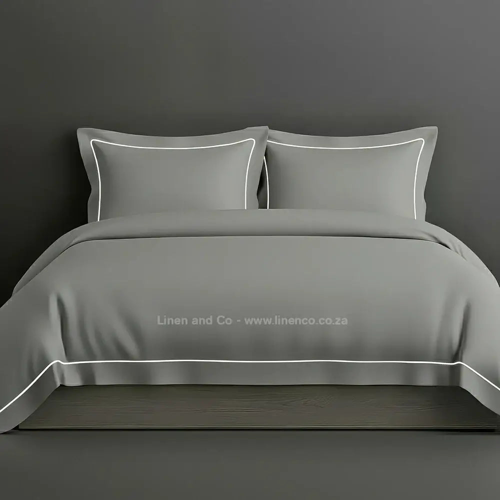 Grey percale duvet cover set with Oxford one-row white satin stitch border from Linen and Co, showcasing elegant hospitality bedding with subtle decorative detailing against a dark grey background.