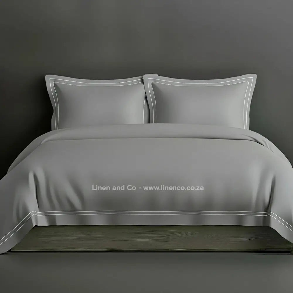 Grey percale duvet cover set with Oxford two-row white satin stitch border from Linen and Co, showcasing elegant hospitality bedding with subtle decorative detailing against a dark grey background.