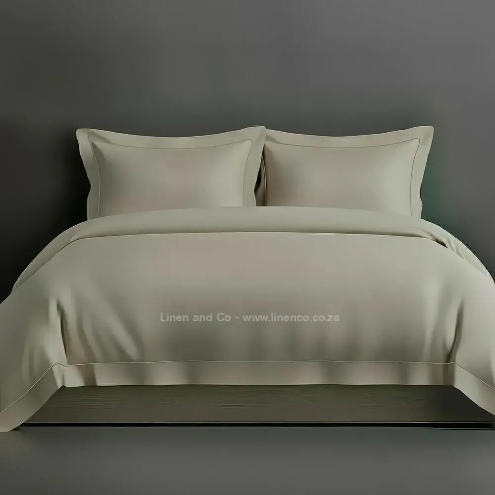 Stone percale duvet cover set with Oxford one-row white satin stitch border from Linen and Co, showcasing elegant hospitality bedding with subtle decorative detailing against a dark grey background.