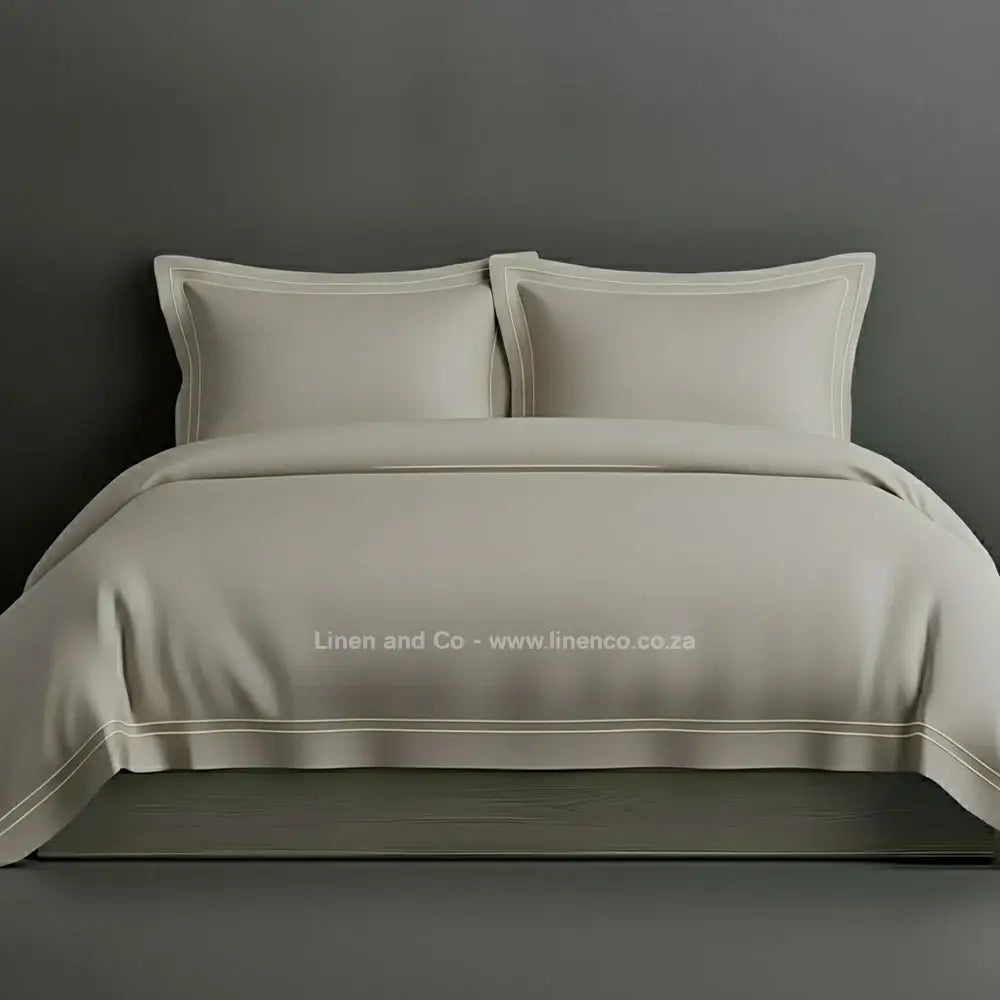 Stone percale duvet cover set with Oxford two-row white satin stitch border from Linen and Co, showcasing elegant hospitality bedding with subtle decorative detailing against a dark grey background.