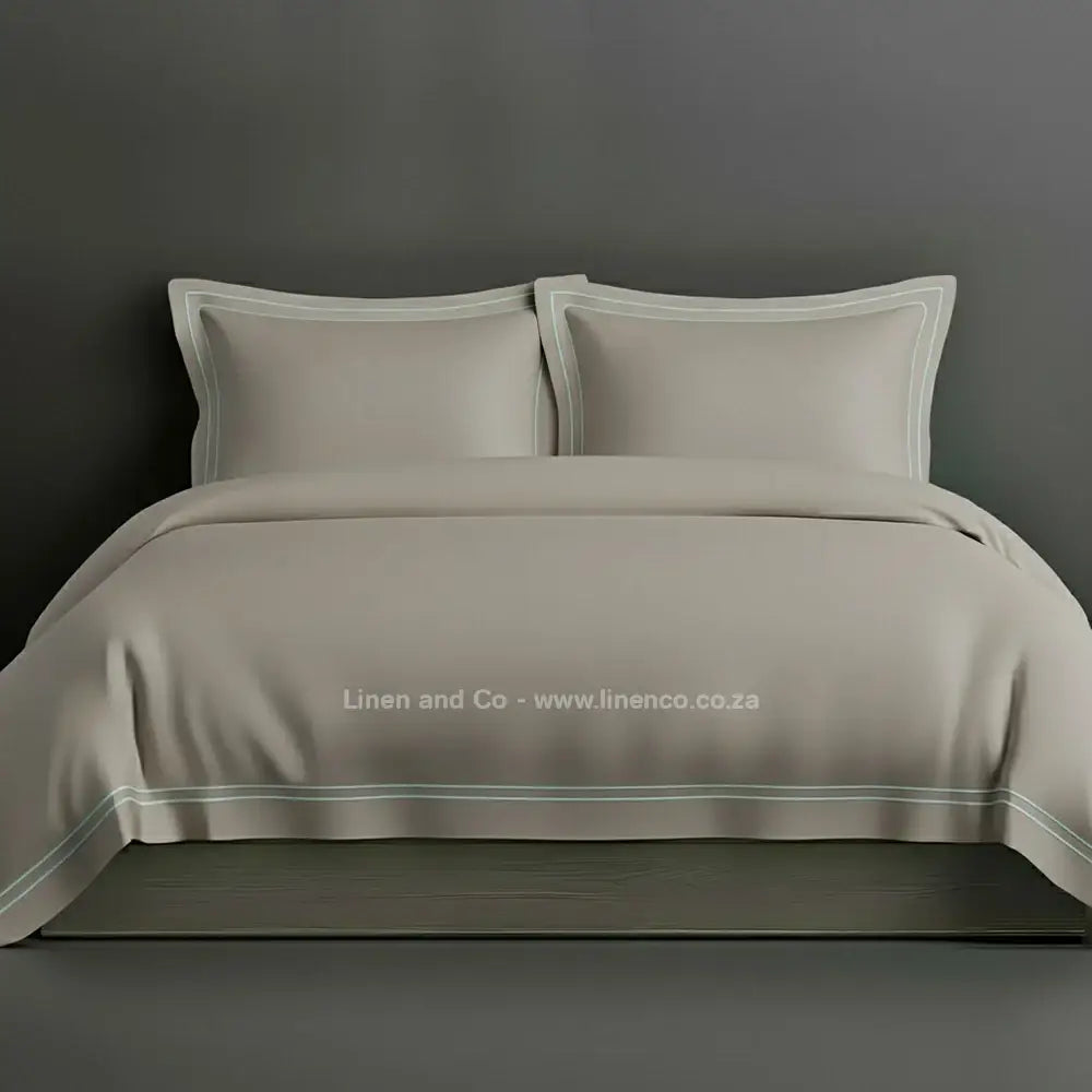 Stone percale duvet cover set with Oxford two-row white satin stitch border from Linen and Co, showcasing elegant hospitality bedding with subtle decorative detailing against a dark grey background.