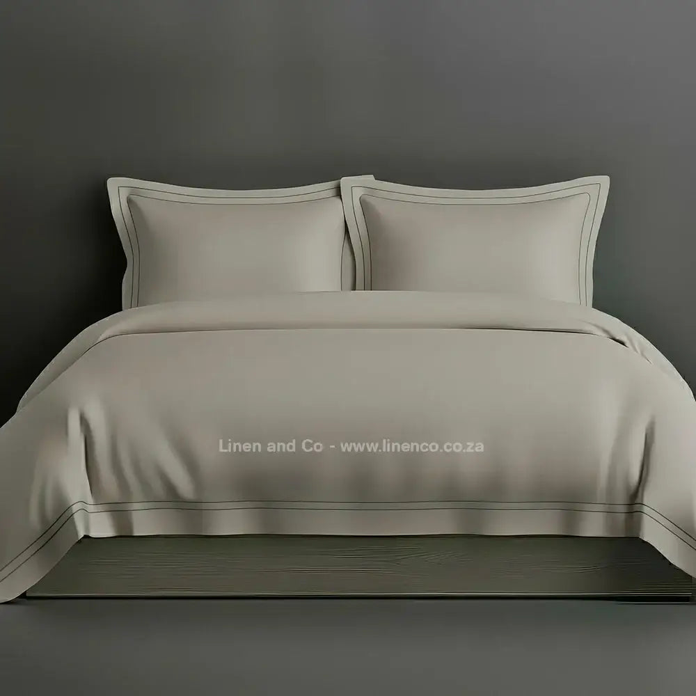 Stone percale duvet cover set with Oxford two-row white satin stitch border from Linen and Co, showcasing elegant hospitality bedding with subtle decorative detailing against a dark grey background.