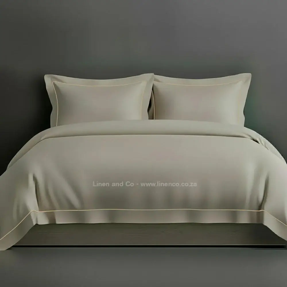 Stone percale duvet cover set with Oxford two-row white satin stitch border from Linen and Co, showcasing elegant hospitality bedding with subtle decorative detailing against a dark grey background.
