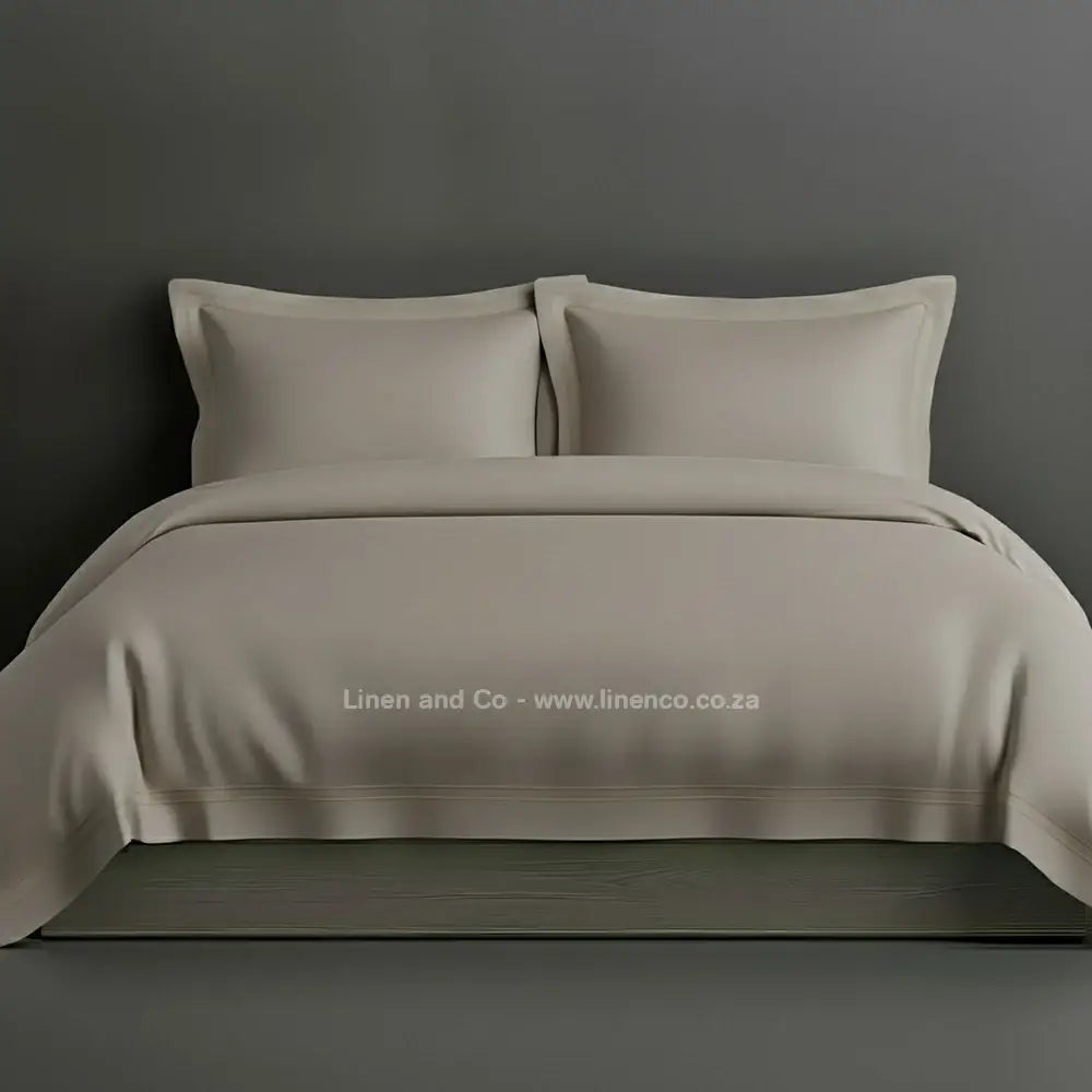 Stone percale duvet cover set with Oxford two-row white satin stitch border from Linen and Co, showcasing elegant hospitality bedding with subtle decorative detailing against a dark grey background.