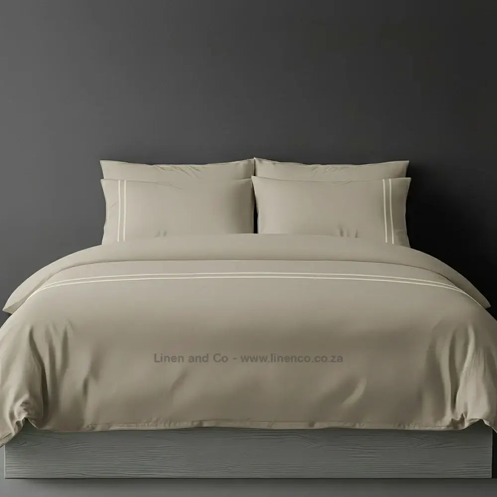 Stone polycotton percale duvet cover set with two-row white satin stitch border from Linen and Co, showcasing elegant hospitality bedding with subtle decorative detailing against a dark grey background.