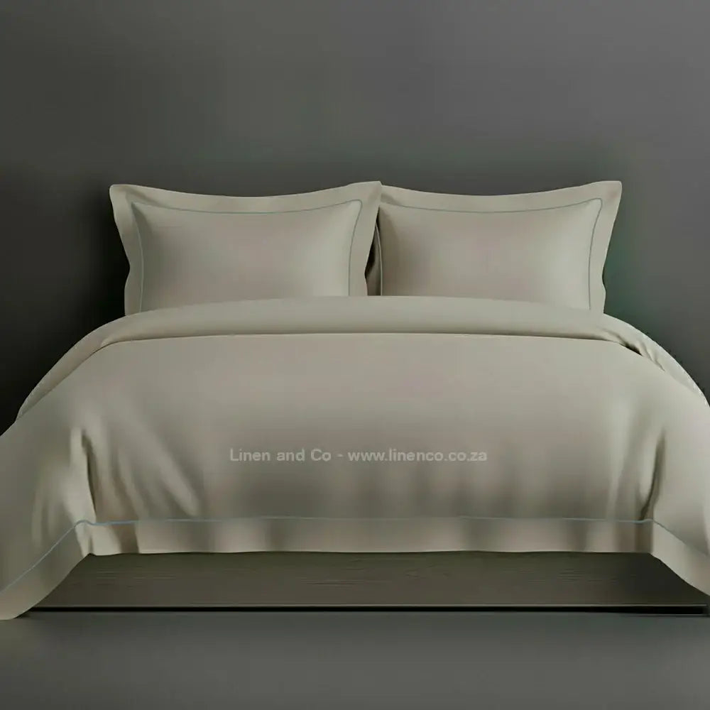 Stone percale duvet cover set with Oxford two-row white satin stitch border from Linen and Co, showcasing elegant hospitality bedding with subtle decorative detailing against a dark grey background.