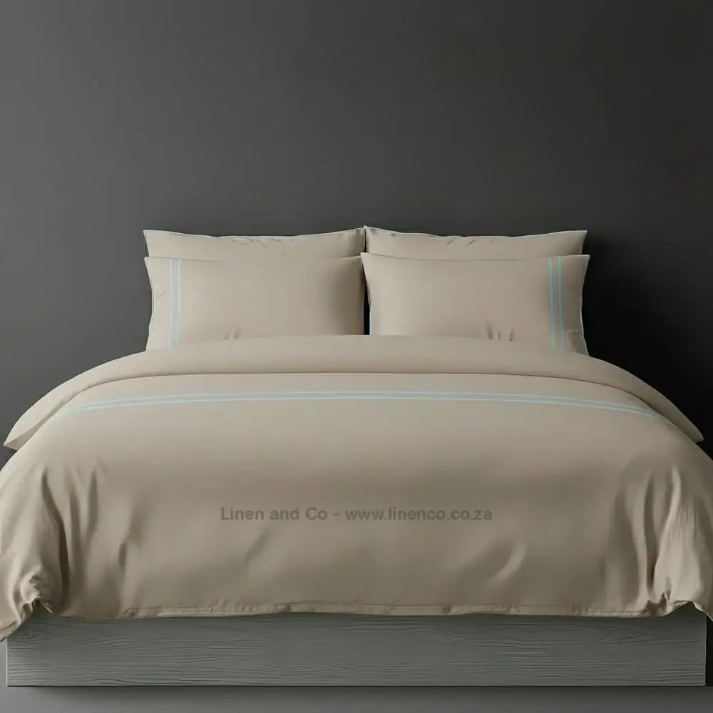 Stone percale duvet cover set with two-row white satin stitch border from Linen and Co, showcasing elegant hospitality bedding with subtle decorative detailing against a dark grey background.
