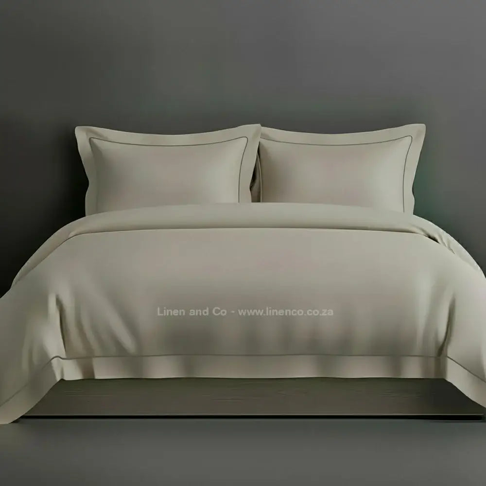 Stone percale duvet cover set with Oxford two-row white satin stitch border from Linen and Co, showcasing elegant hospitality bedding with subtle decorative detailing against a dark grey background.