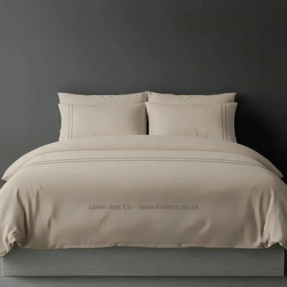 Stone percale duvet cover set with two-row white satin stitch border from Linen and Co, showcasing elegant hospitality bedding with subtle decorative detailing against a dark grey background.
