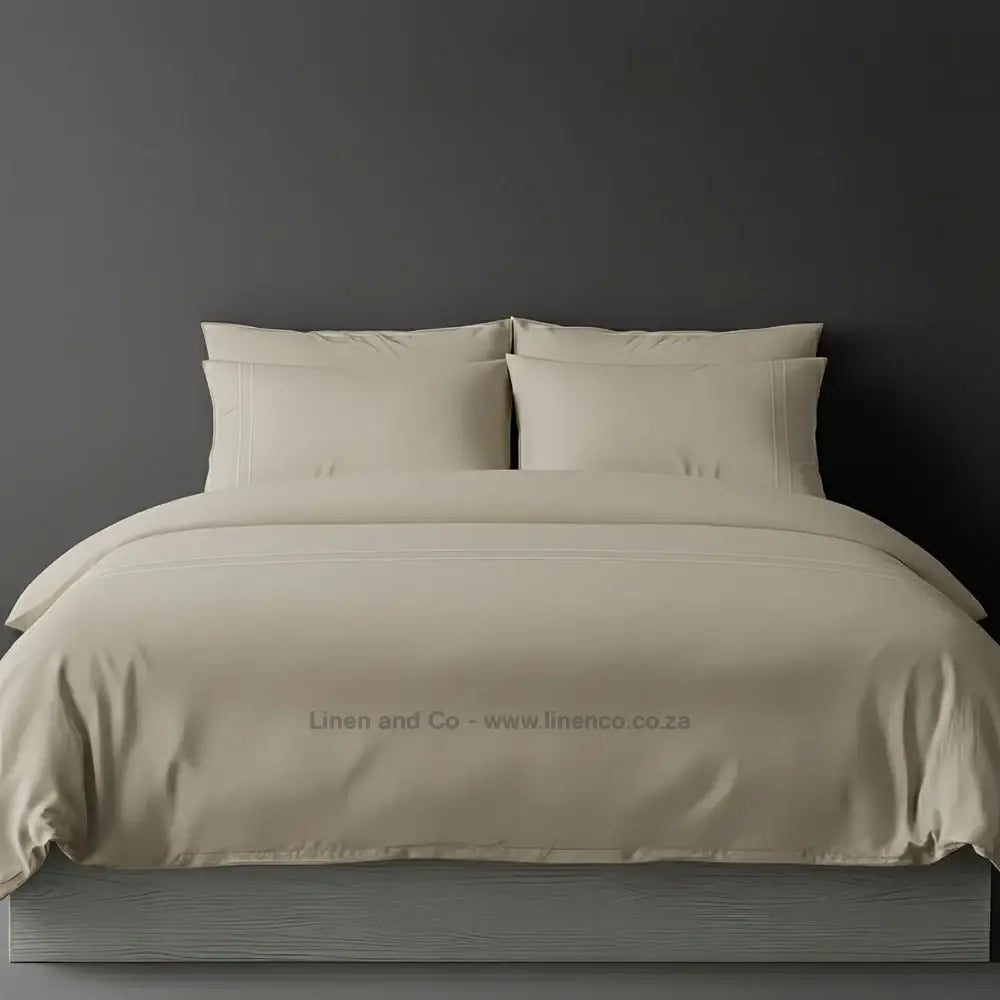 Stone percale duvet cover set with two-row white satin stitch border from Linen and Co, showcasing elegant hospitality bedding with subtle decorative detailing against a dark grey background.