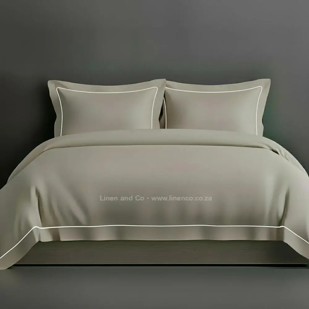 Stone percale duvet cover set with Oxford two-row white satin stitch border from Linen and Co, showcasing elegant hospitality bedding with subtle decorative detailing against a dark grey background.