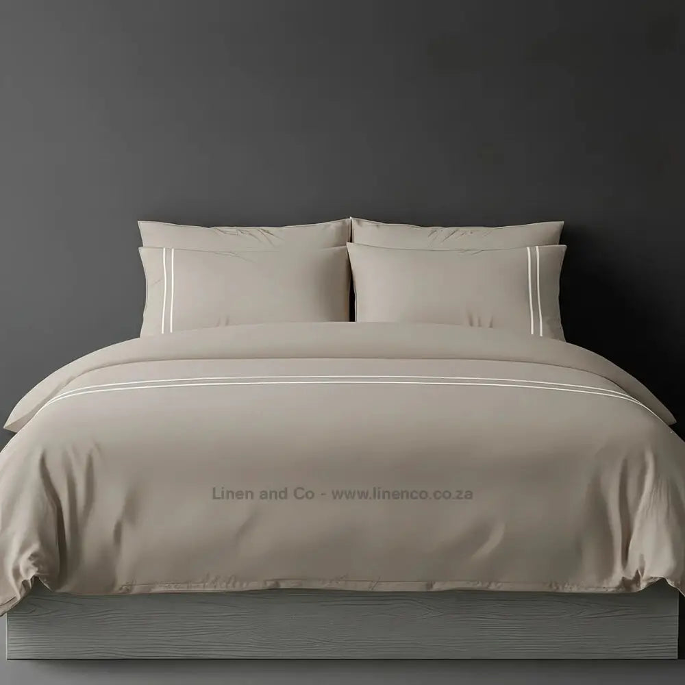 Stone percale duvet cover set with two-row white satin stitch border from Linen and Co, showcasing elegant hospitality bedding with subtle decorative detailing against a dark grey background.