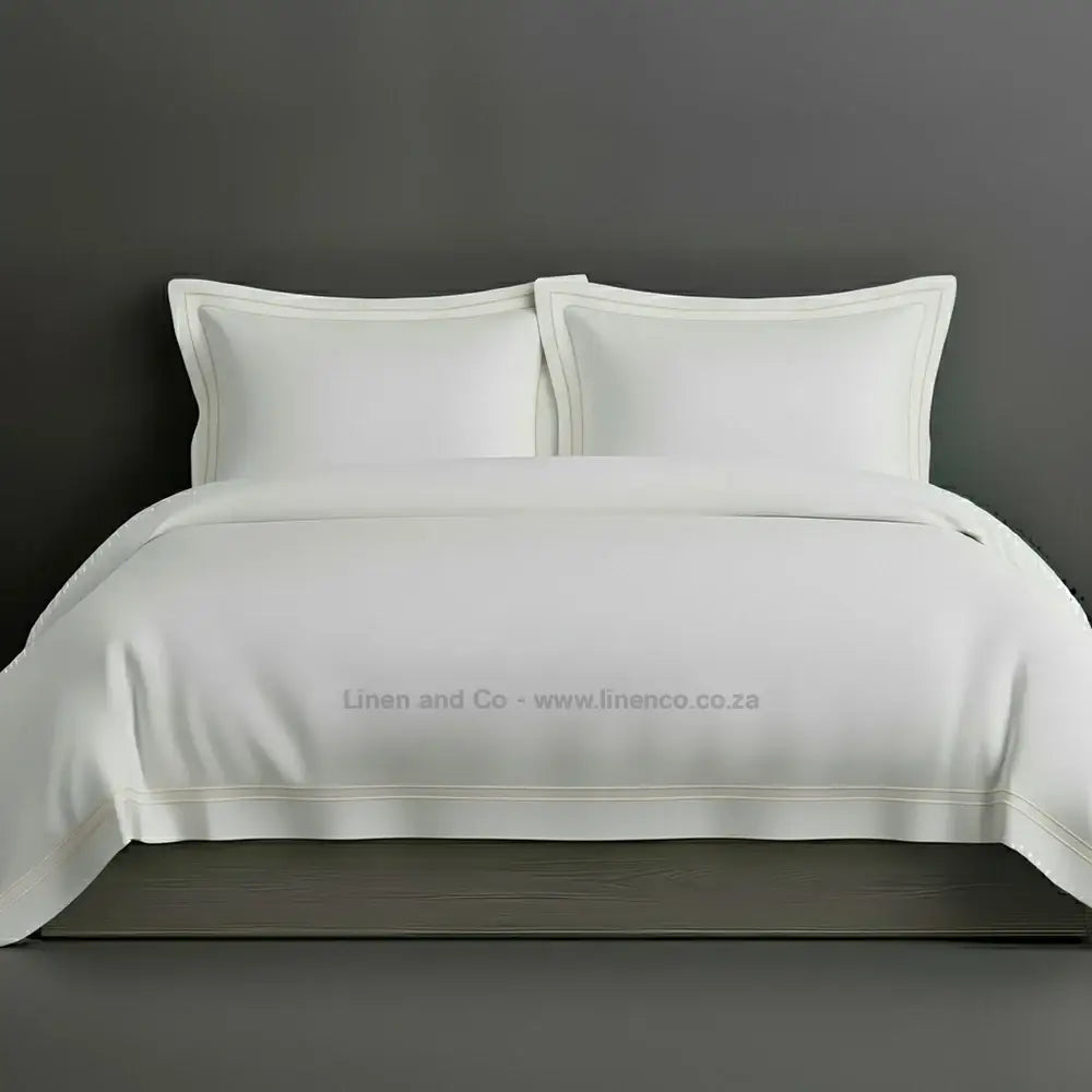 White percale duvet cover set with Oxford two-row white satin stitch border from Linen and Co, showcasing elegant hospitality bedding with subtle decorative detailing against a dark grey background.