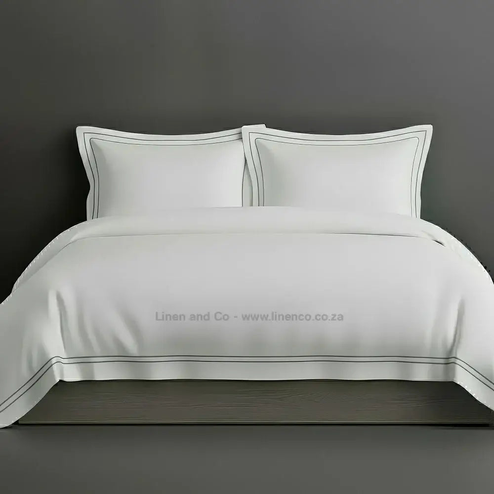 White percale duvet cover set with Oxford two-row white satin stitch border from Linen and Co, showcasing elegant hospitality bedding with subtle decorative detailing against a dark grey background.