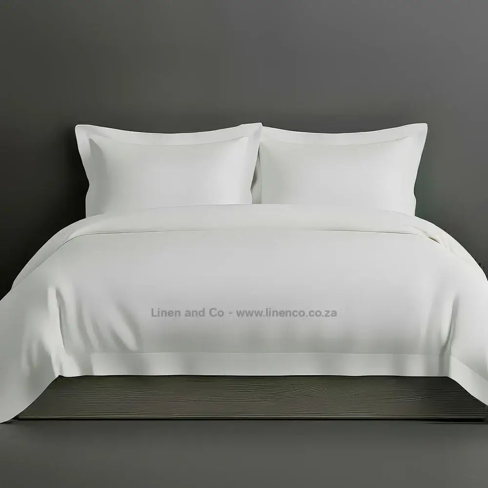 White percale duvet cover set with Oxford border from Linen and Co, showcasing elegant hospitality bedding with against a dark grey background.