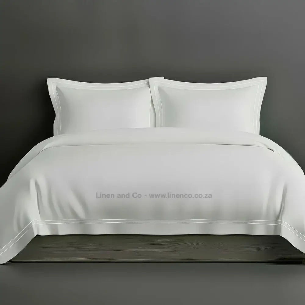 White percale duvet cover set with Oxford two-row white satin stitch border from Linen and Co, showcasing elegant hospitality bedding with subtle decorative detailing against a dark grey background.