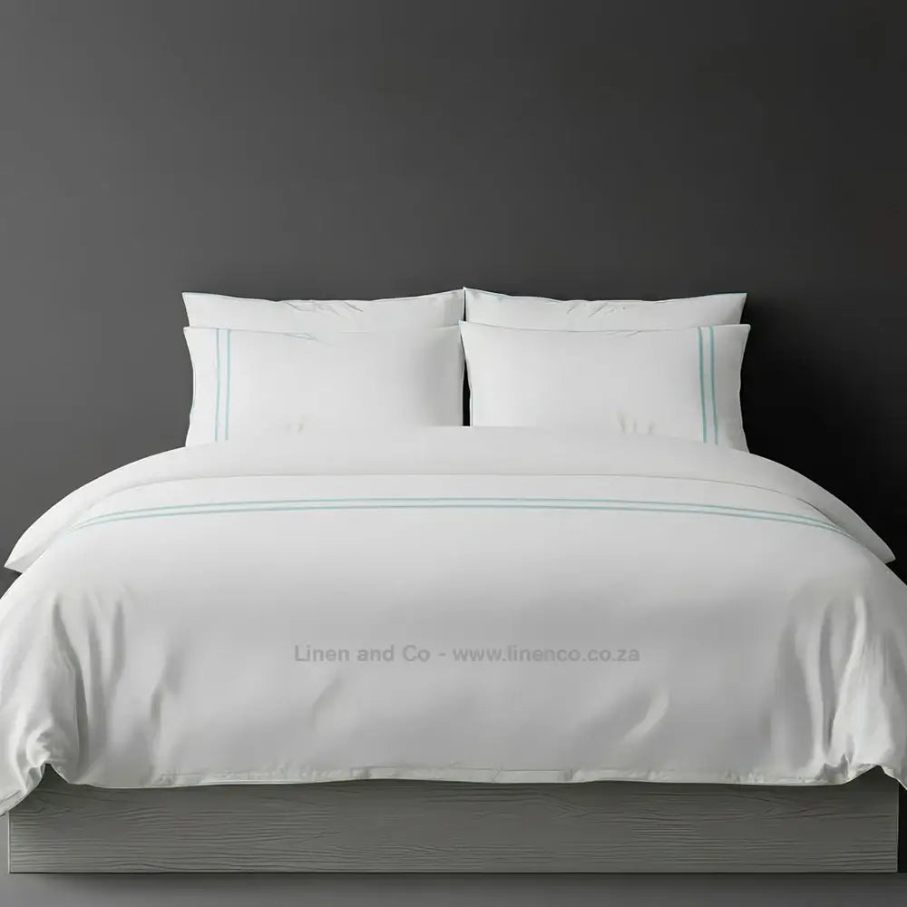 White polycotton percale duvet cover set with two-row white satin stitch border from Linen and Co, showcasing elegant hospitality bedding with subtle decorative detailing against a dark grey background