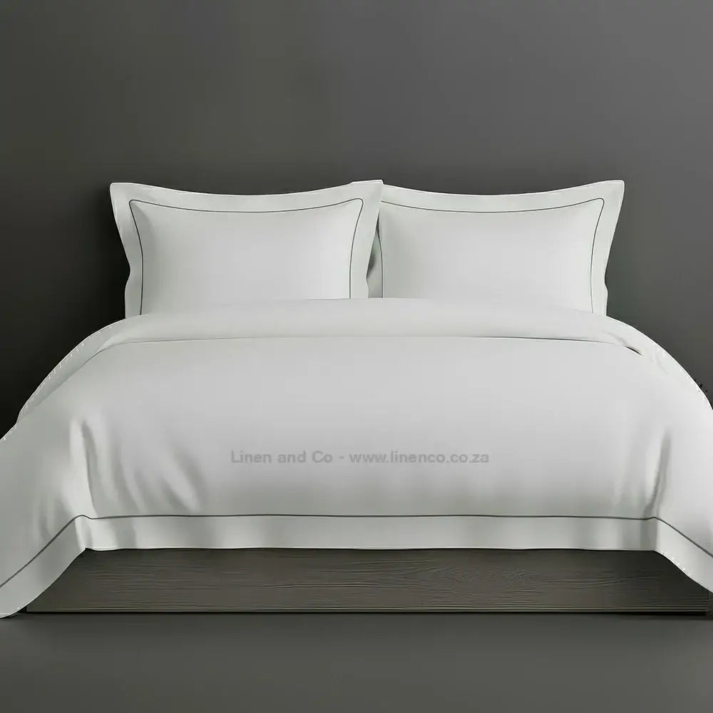 White percale duvet cover set with Oxford two-row white satin stitch border from Linen and Co, showcasing elegant hospitality bedding with subtle decorative detailing against a dark grey background.