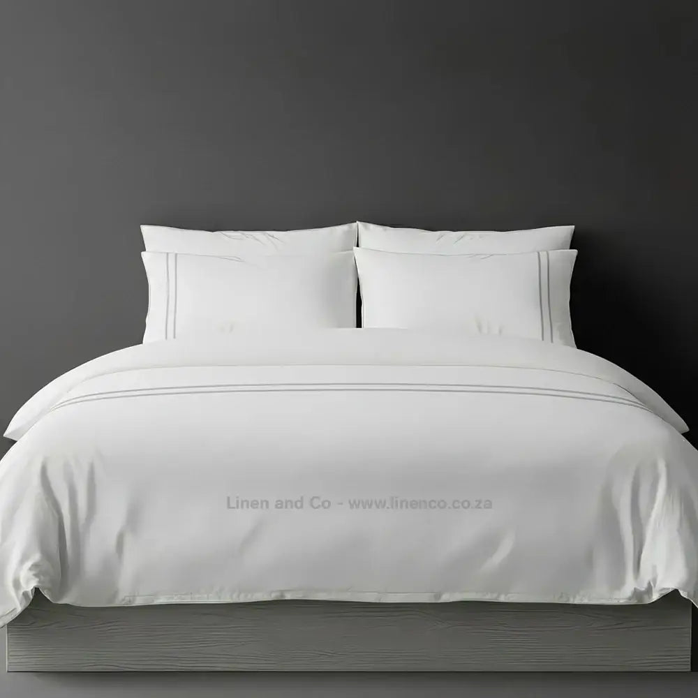 White percale duvet cover set with two-row white satin stitch border from Linen and Co, showcasing elegant hospitality bedding with subtle decorative detailing against a dark grey background