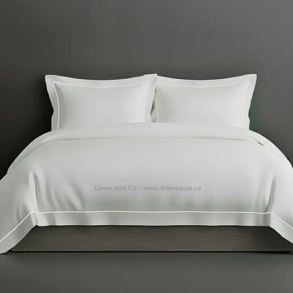 White percale duvet cover set with Oxford two-row white satin stitch border from Linen and Co, showcasing elegant hospitality bedding with subtle decorative detailing against a dark grey background.