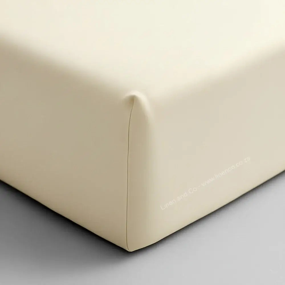 Cream fitted sheet corner on mattress showing elastic edge and smooth percale fabric - Linen & Co hospitality bedding