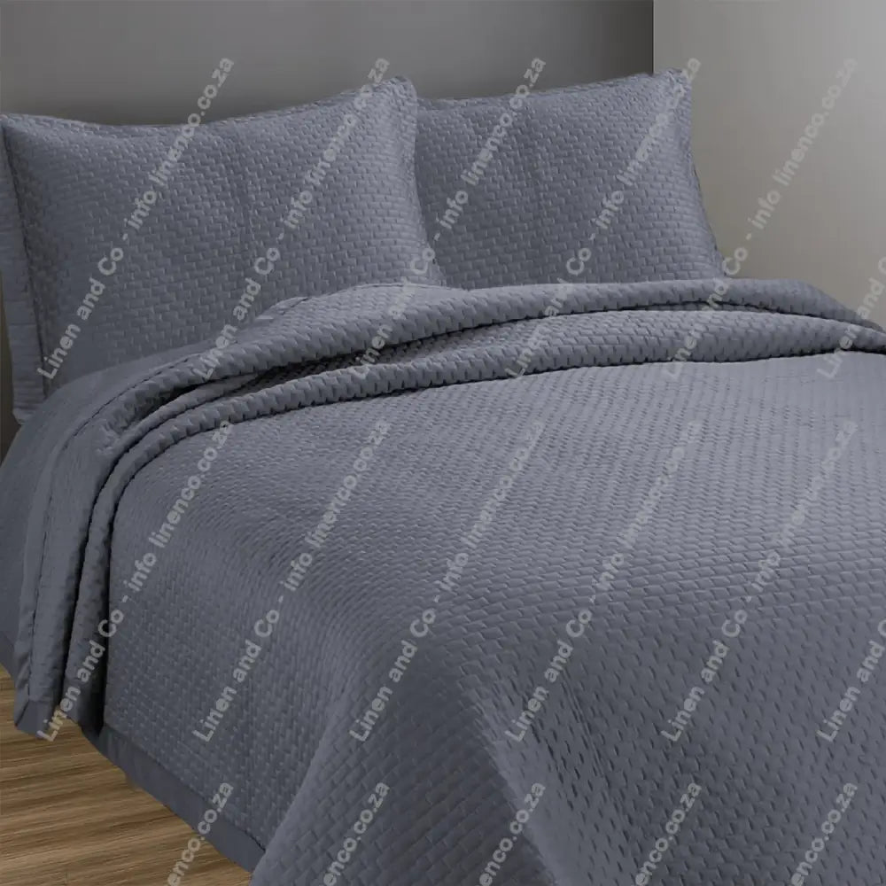 Grey Berlin design quilted bedspread with matching pillow cases on a bed.