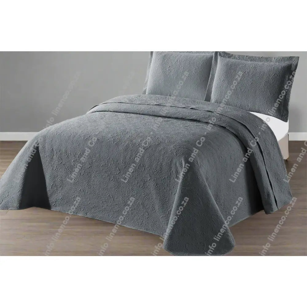 Grey Daisy Design Quilted bedspread on a bed with a grey wall background