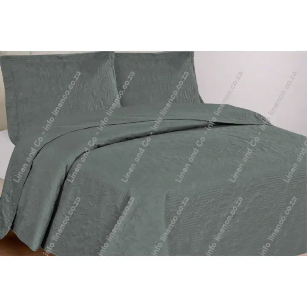 Grey Melissa Design textured quilt and pillow set on a bed in a bedroom setting.