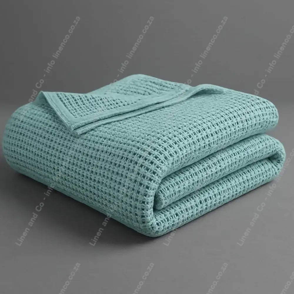 Linen and Co Duck Egg Cotton Cellular blanket folded on a grey background