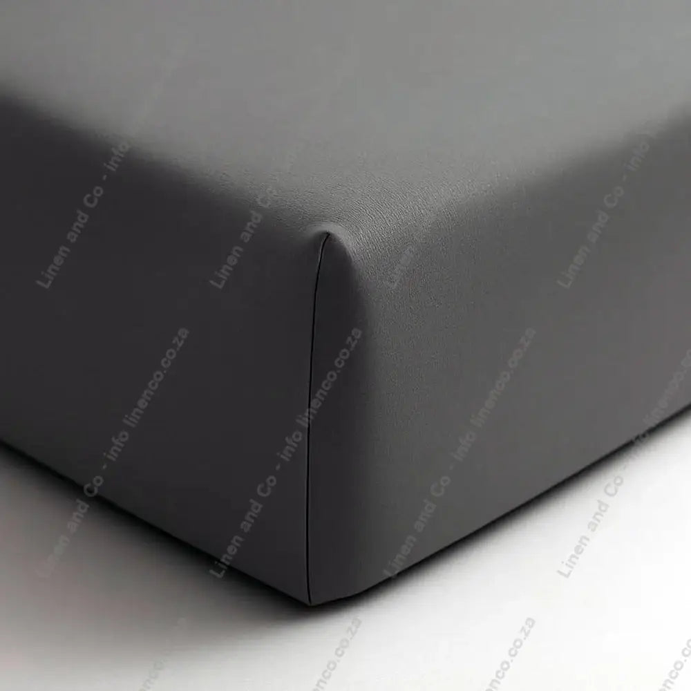 Gray fitted sheet on a bed corner with a plain background