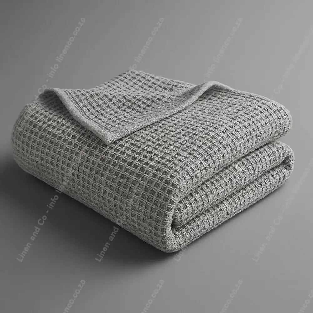 Linen and Co Light Grey Cotton Cellular blanket folded on a grey background