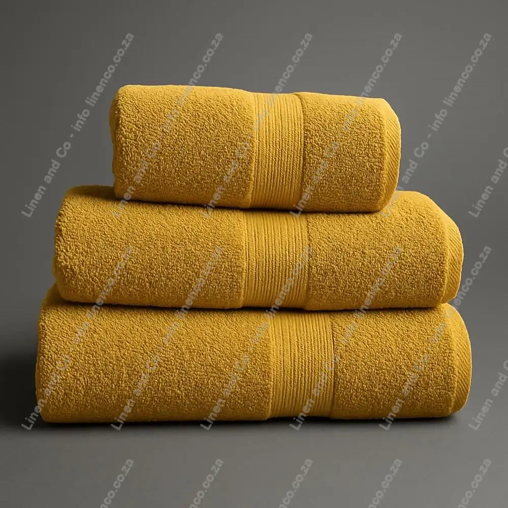 Linen and Co - Stack of three Mustard Egyptian 450gsm towels stacked on a grey background.