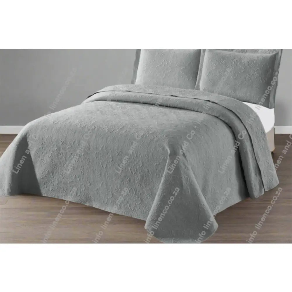 Platinum Daisy Design Quilted bedspread on a bed with a grey wall background